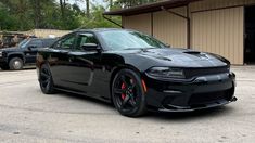 a black dodge charger is parked in front of a building with other vehicles behind it