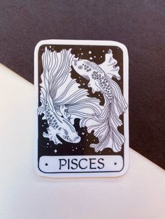 a white and black sticker with two fish in it's body, on top of a table