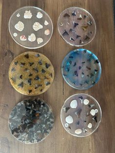 four glass plates with shells on them sitting on a wooden table next to each other