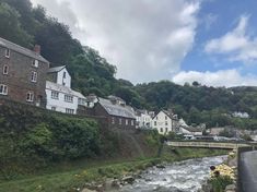 a river running through a lush green hillside next to tall buildings on top of a hill