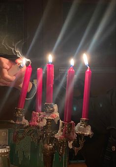 a person lighting candles on a table with other items in front of them and the light coming from one candle