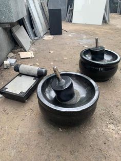 two large black bowls sitting on top of a dirt ground next to a cement box