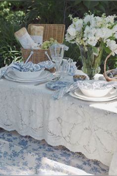 a table set for two with plates and flowers in vases on the table cloth