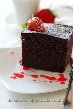 a piece of chocolate cake on a white plate with strawberries and sauce drizzled around it