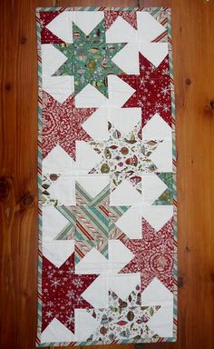 a quilted table runner with red, green and white stars on the top is sitting on a wooden surface