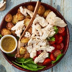 a bowl filled with chicken, potatoes and tomatoes next to a small bowl of dressing