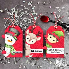 three tags with snowman and reindeer on them next to some silver glittery beads