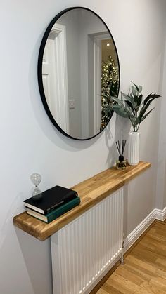 a mirror on the wall above a wooden shelf with a book and potted plant