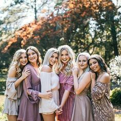 a group of women standing next to each other posing for a photo in front of trees