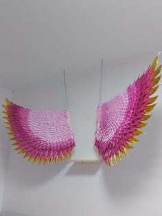 two pink and yellow wings hanging from the ceiling in a room with white wallpaper