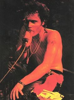 a shirtless man holding a microphone in his right hand and sitting on the ground