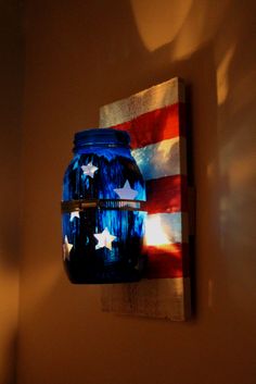 a blue mason jar is hanging on the wall next to a light fixture with an american flag painted on it