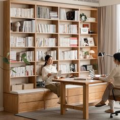 two women sitting at a desk in front of a book shelf with books on it