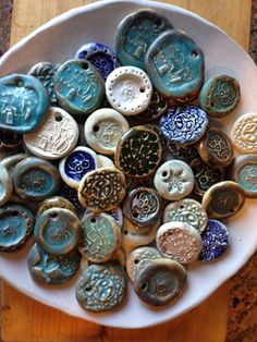 a white bowl filled with lots of different colored buttons on top of a wooden table