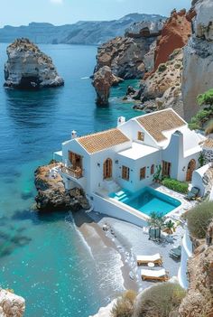 an aerial view of a white house on the beach with blue water and cliffs in the background