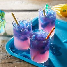 two glasses filled with blue and pink liquid sitting on a tray next to an umbrella