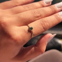 a woman's hand with a gold ring and green gems on it, while she is wearing white nail polish