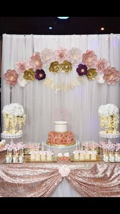 a table topped with cake and cupcakes under a flower covered wall hanging from the ceiling