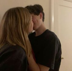 a young man and woman kissing in front of a white door with the light shining on them