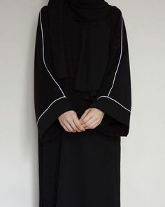 a woman wearing a black hijab standing in front of a white wall with her hands on her hips