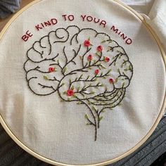 a hand embroidered brain on a white cloth with red and green stitching that says, be kind to your mind