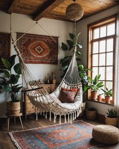 a hammock hanging from the ceiling in a room with potted plants and rugs