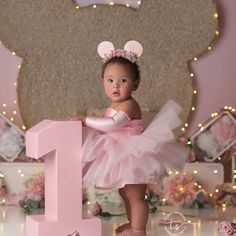 a baby girl in a pink tutu standing next to the number one