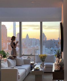 a woman standing in a living room next to a large window looking out at the city