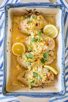 chicken with lemons, corn and herbs in a blue dish on a striped cloth