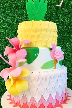 a three tiered cake decorated with flowers and pineapples is on a table