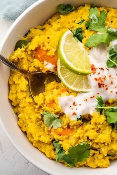 a white bowl filled with rice and garnished with cilantro, lime wedges and sour cream