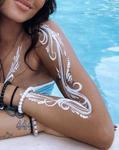 a woman with white paint on her body sitting next to a swimming pool wearing bracelets