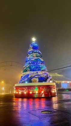 a brightly lit christmas tree in the middle of a parking lot at night with lights on it