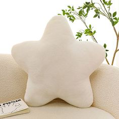 a white star shaped pillow sitting on top of a couch next to a book and a potted plant