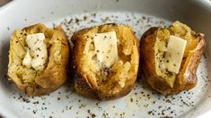 three baked potatoes with butter and seasoning in a white bowl