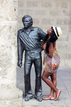 a woman standing next to a statue of a man with a hat on his head