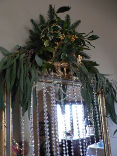 a mirror hanging on the wall with beads and greenery in it's reflection