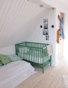 there is a green crib in the corner of this room with white walls and wood floors