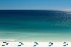 several umbrellas are set up on the beach in front of an ocean and clear blue sky