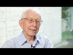 an older man wearing glasses and a blue shirt is smiling at the camera while he sits in front of a chain link fence