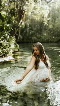 a pregnant woman sitting in the middle of a river with her hands on her hips