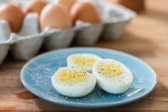 three hard boiled eggs on a blue plate next to an egg carton filled with eggs