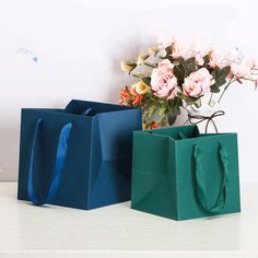 two bags with handles are sitting on a table next to a vase filled with flowers