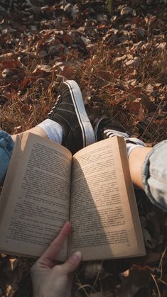 someone is reading a book on the ground with their legs crossed and one hand holding an open book