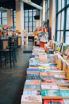 many books are lined up on the table in front of large windows and tables with chairs