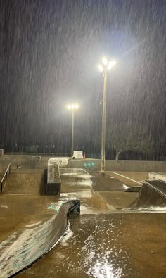 an empty skate park at night with the lights on and rain falling all around it