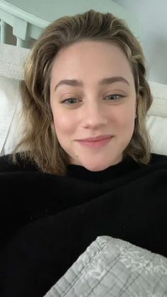 a woman laying in bed with her eyes closed and looking at the camera while wearing a black sweater