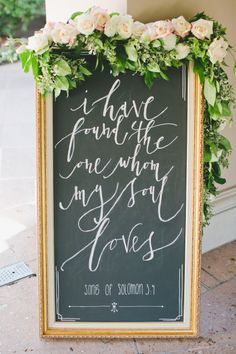 a chalkboard sign decorated with flowers and greenery