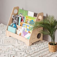 a wooden book holder with books and magazines in it next to a potted plant