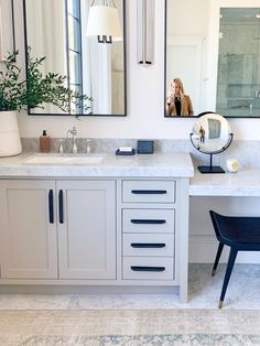 a white bathroom with two mirrors and a vanity in front of the mirror is a blue chair